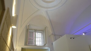 Una habitación con techo alto, una ventana con persianas y una lámpara.