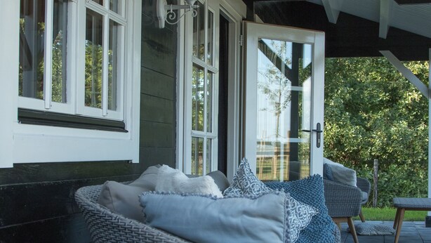 A covered outdoor seating area with wicker furniture and a white door. - House Halfway to Veere (Veere)