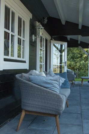 A covered outdoor seating area with wicker furniture and a white door. - House Halfway to Veere (Veere)