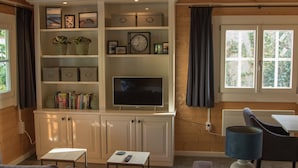 A living room with a TV, shelves with books and plants, a table with a remote, and a window with curtains. - House Halfway to Veere (Veere)