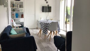 A modern living room with a sofa, a dining table with chairs, a bookshelf, and a TV mounted on the wall. - Nice Capbretonnaise three rooms between port, trade, and beach (Capbreton)