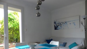 A bright room with a white table, blue mats, a white sofa with blue cushions, and a painting of boats on the wall. - Nice Capbretonnaise three rooms between port, trade, and beach (Capbreton)
