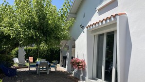 A patio area with outdoor furniture, a tree, and a white building with a window. - Nice Capbretonnaise three rooms between port, trade, and beach (Capbreton)
