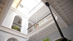 A multi-level atrium with white walls, a balcony with a metal railing, and a hanging light fixture. - Casa Patio del Panadero (Cádiz)