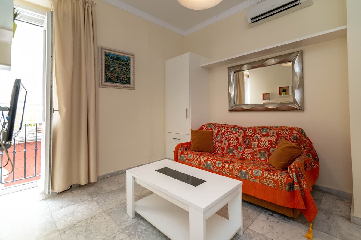A room with a patterned sofa, a white coffee table, a mirror, and a door with curtains.