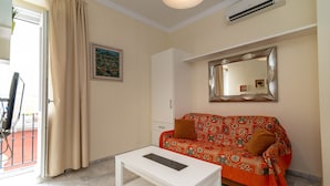 A room with a patterned sofa, a white coffee table, a mirror, and a door with curtains. - Casa Patio del Panadero (Cádiz)