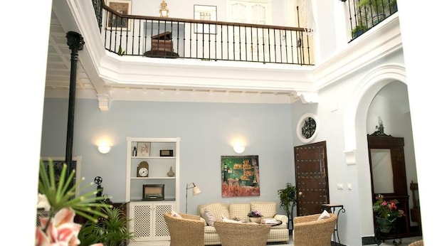 A spacious living area with a high ceiling, a balcony with a railing, and a large painting on the wall. - Casa Patio del Panadero (Cádiz)