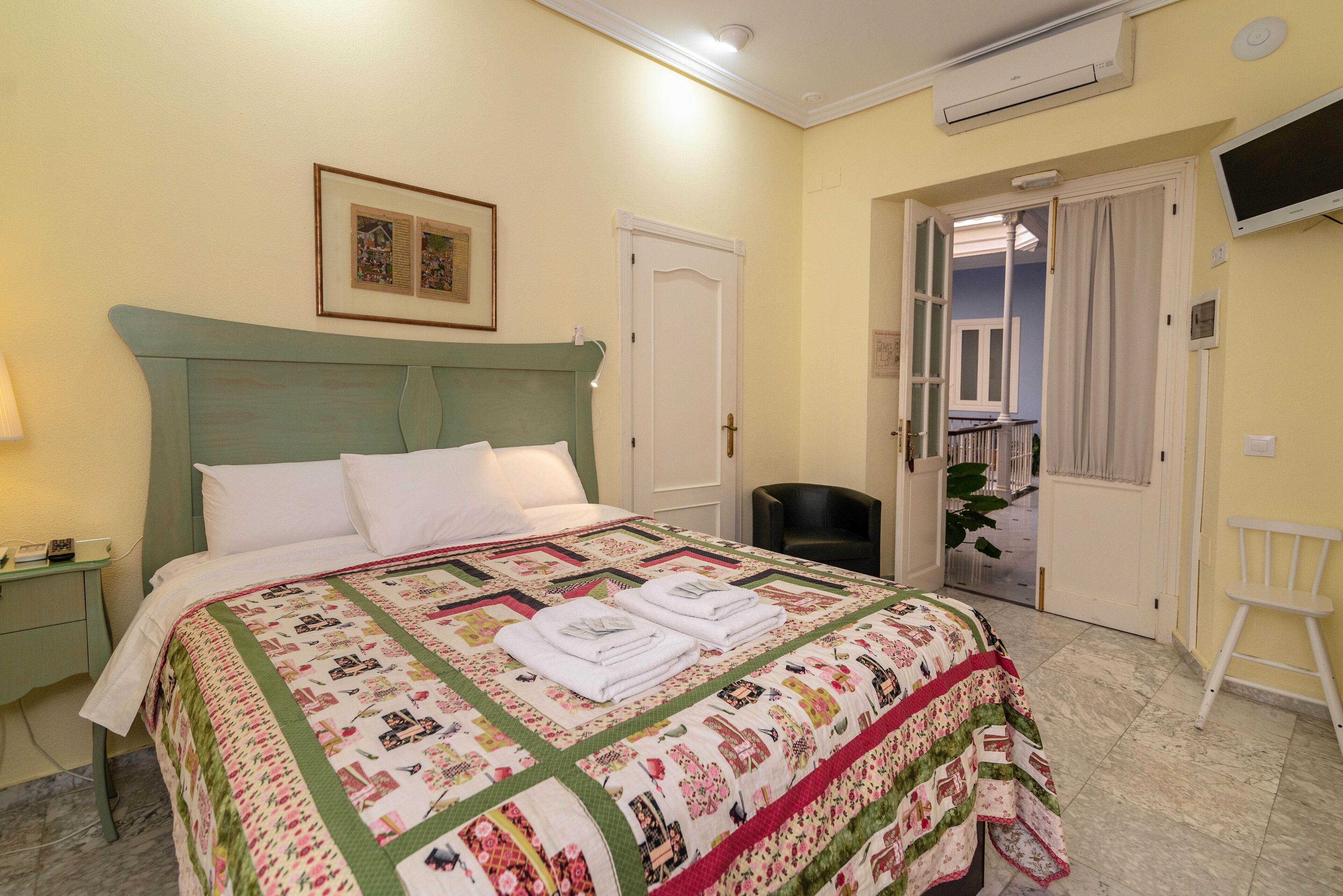 A neatly made bed with a quilt, a bedside table with a lamp, and a door leading to another room.
