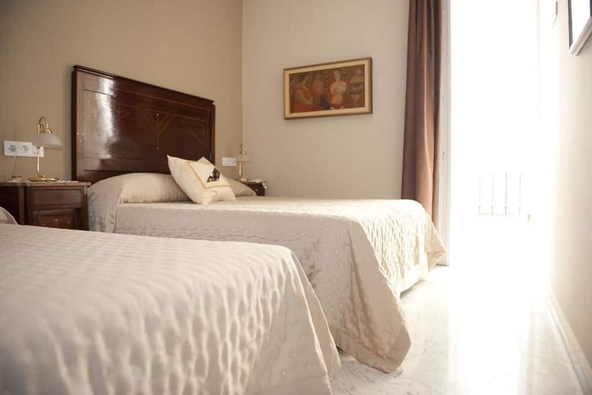 A hotel room with two beds, a wooden headboard, a nightstand, a lamp, and a painting on the wall.