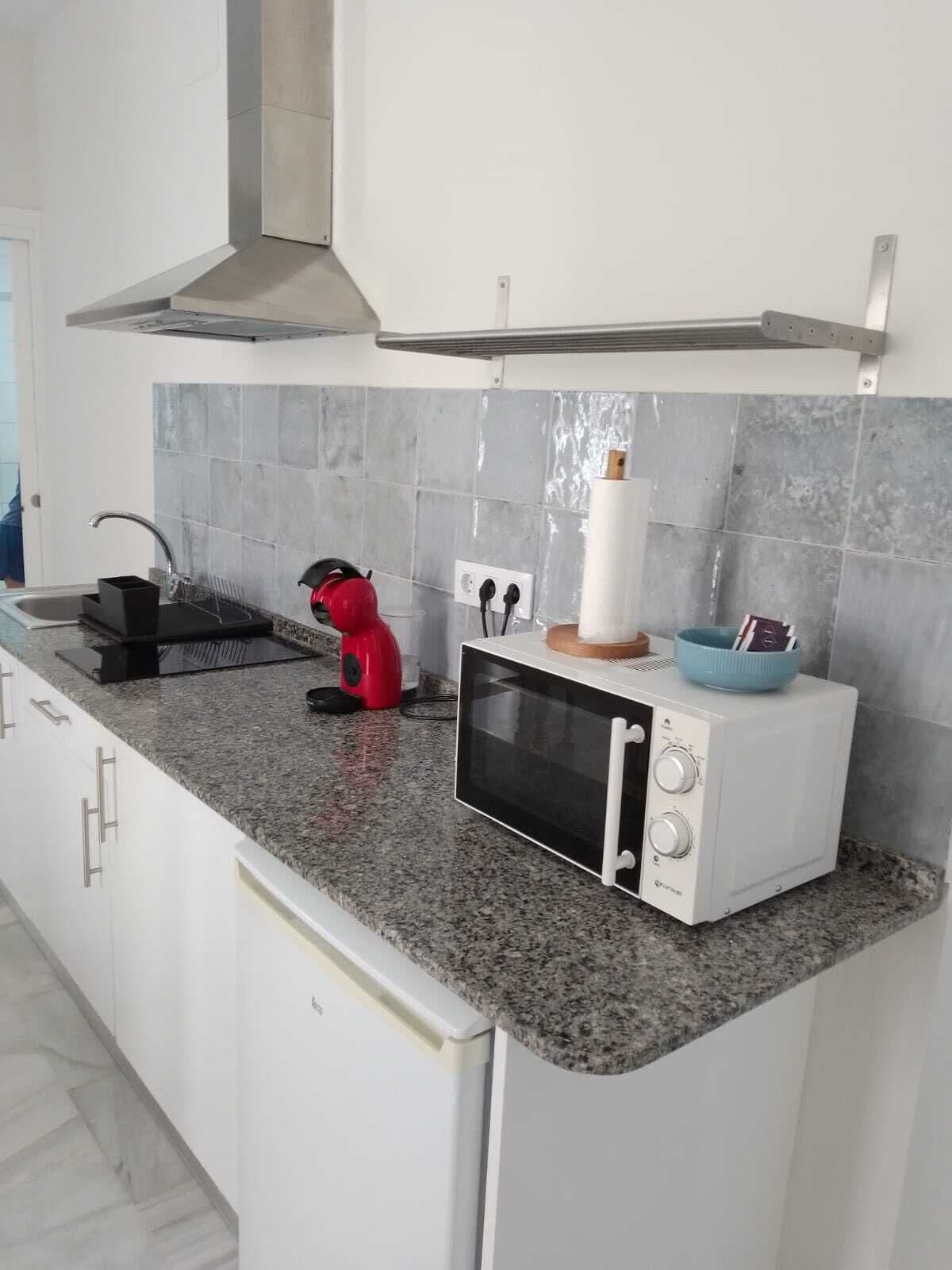 A kitchen with a microwave, a red kettle, and a blue bowl on the countertop.