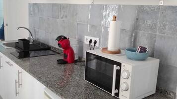 A kitchen with a microwave, a red kettle, and a blue bowl on the countertop.