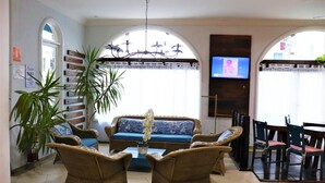 Eine Lobby mit Korbmöbeln, einer blauen Sitzsofa, einem Blumentopf und einem an der Wand hängenden Fernseher.