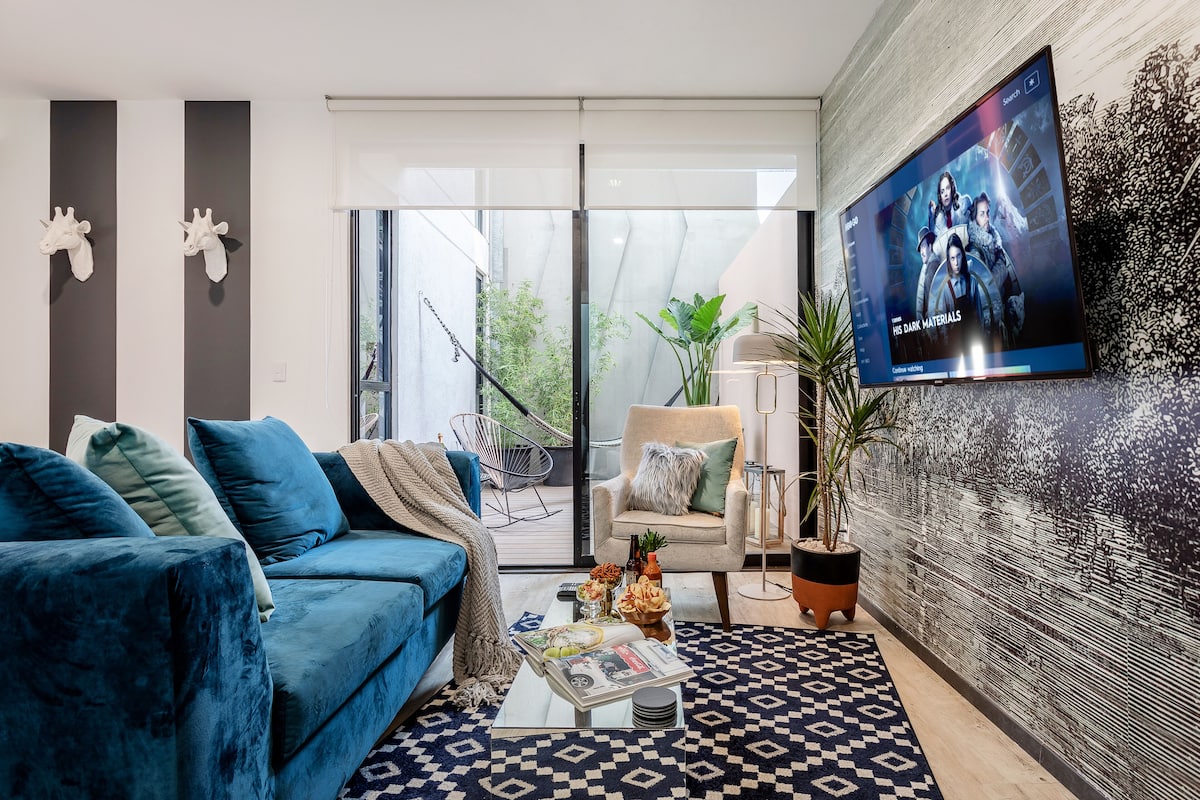 Ein modernes Wohnzimmer mit einem blauen Sofa, einem Couchtisch mit Zeitschriften und einem an der Wand befestigten Fernseher.