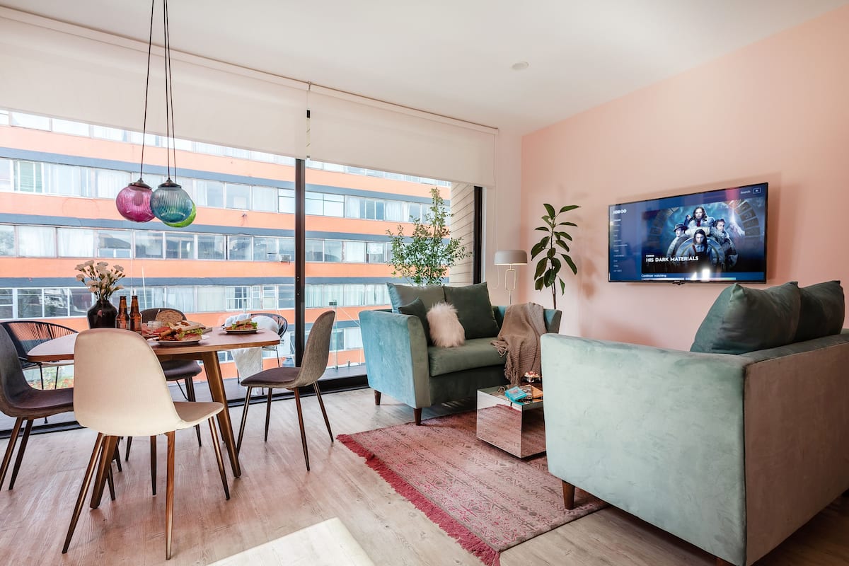 Ein modernes Wohnzimmer mit einer Couch, einem Esstisch, Stühlen und einem Fernseher an der Wand.