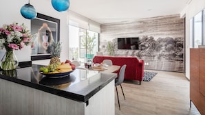 A modern kitchen with a central island, a dining area with a red sofa, and a large TV mounted on a textured wall. - Illumé Urban Living - Apartments in the heart of Roma Norte (Mexico City)