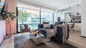 A modern living room with a sofa, coffee table, and a large window offering a view of buildings. - Illumé Urban Living - Apartments in the heart of Roma Norte (Mexico City)