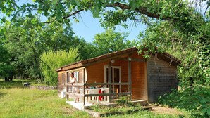 A wooden cabin with a porch, surrounded by greenery. - Accès Piscine, Fitness, Sauna ! Maisonnette Climatisée avec Terrasse (Gramat)