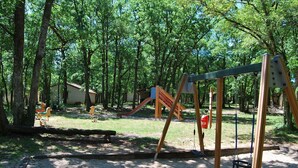 A playground with swings, slides, and a small building in a wooded area. - Accès Piscine, Fitness, Sauna ! Maisonnette Climatisée avec Terrasse (Gramat)