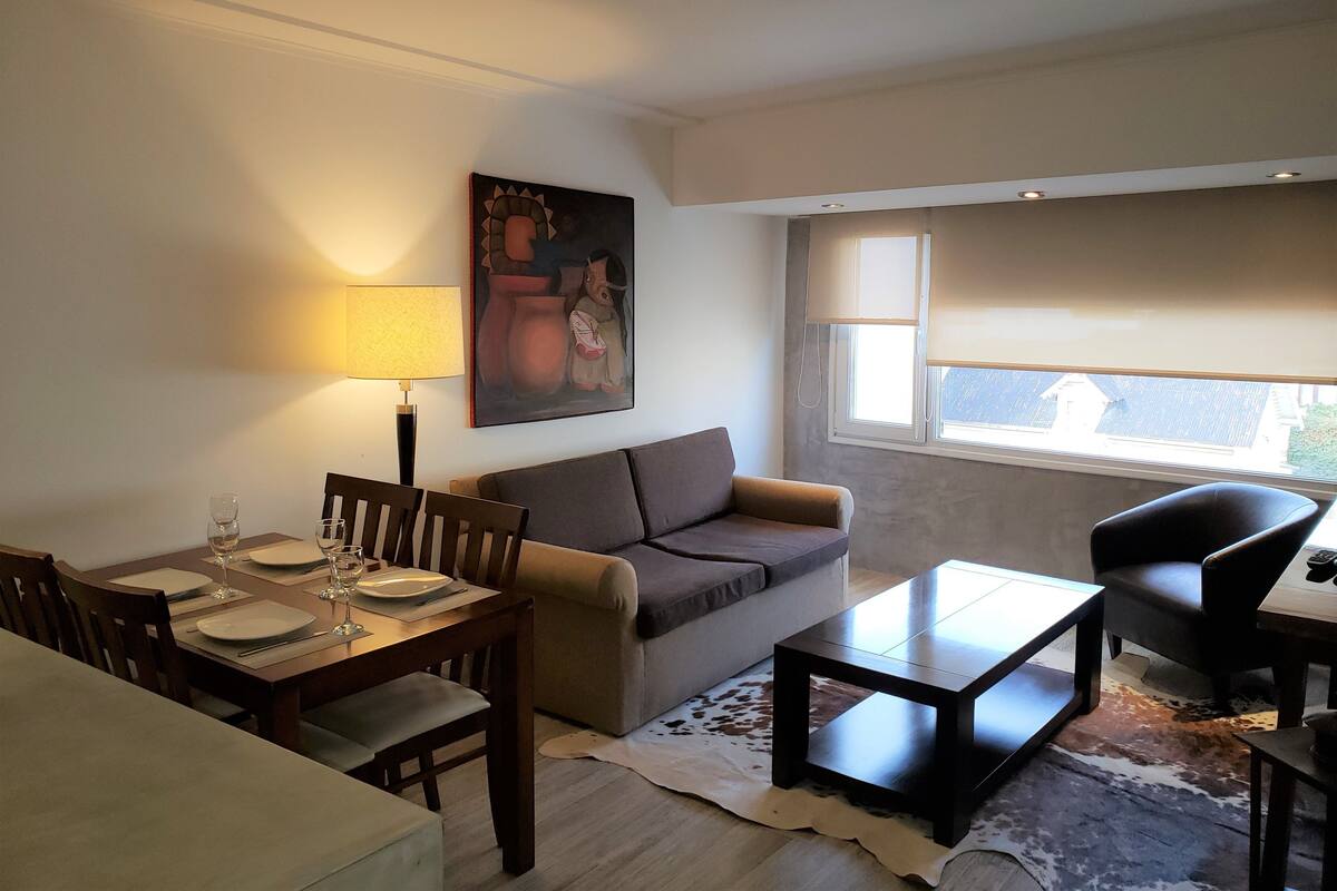 Una sala de estar con comedor, un sofá, una mesa de centro y un cuadro en la pared.