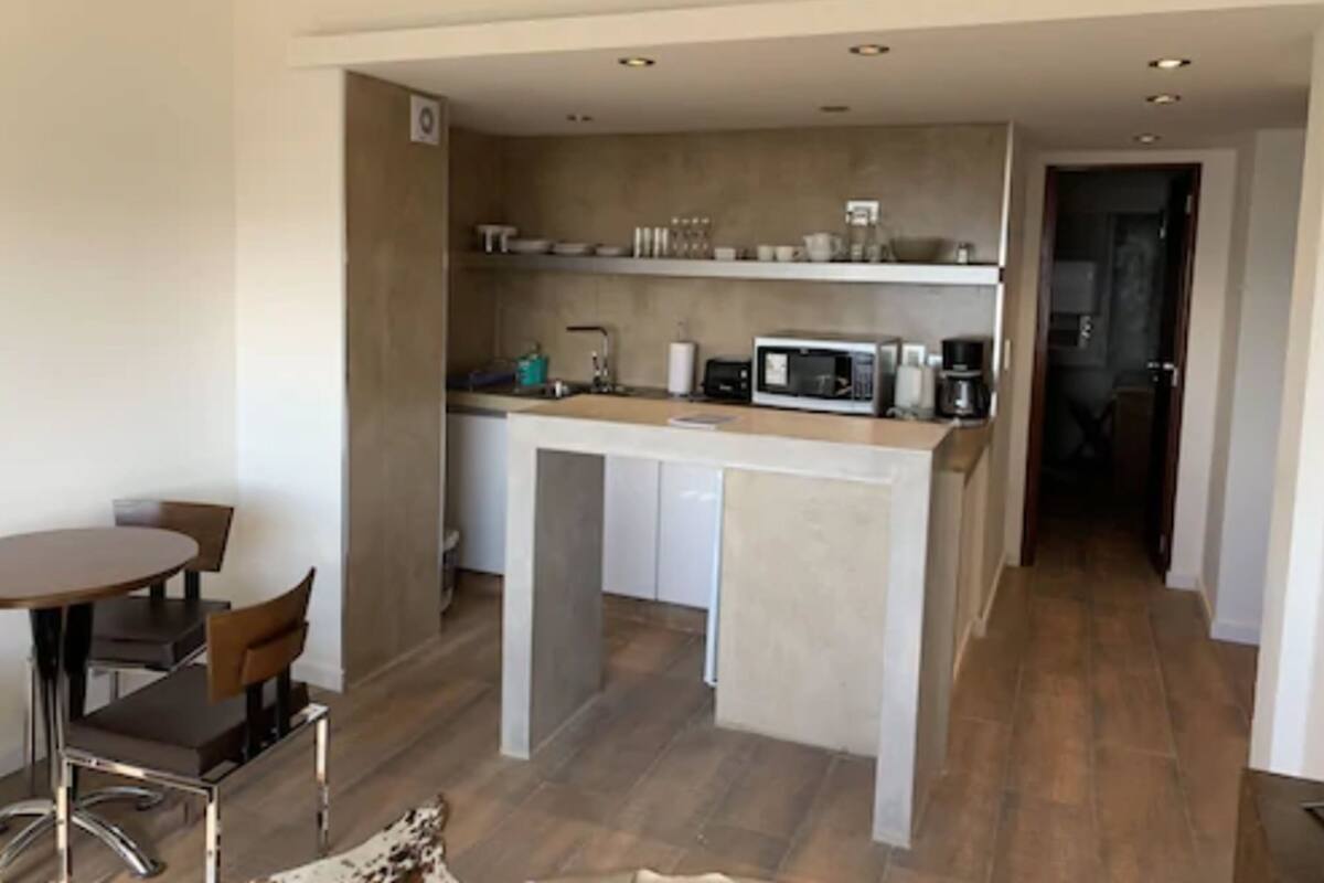 Una cocina moderna con una isla central, armarios blancos y un microondas. Hay un comedor con una mesa redonda y sillas.