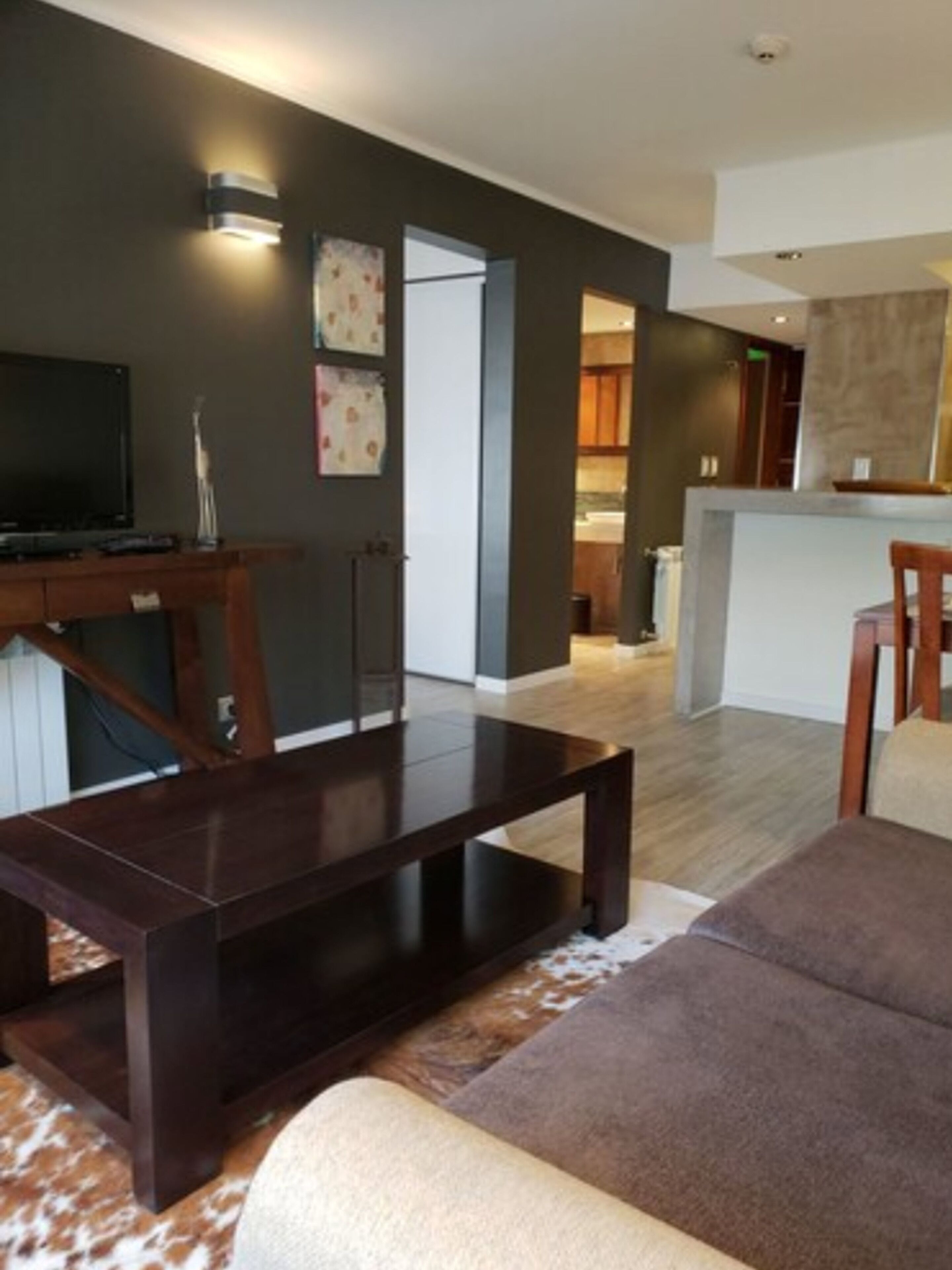 A modern living room with a dark wooden coffee table, a brown sofa, and a television on a wooden stand.