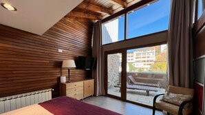 Una camera da letto con un letto, una cassettiera, una TV e un balcone con una sedia.