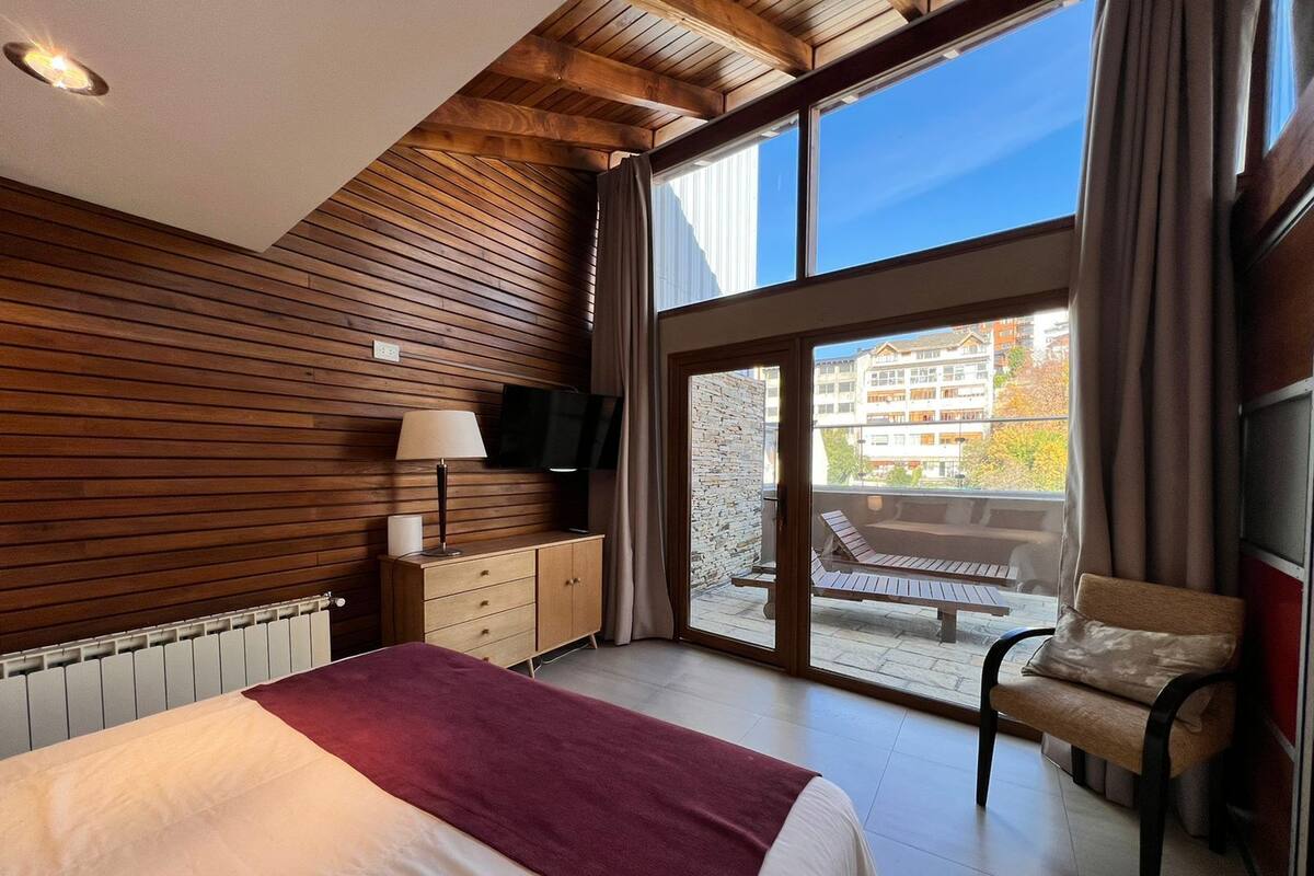 Un dormitorio con cama, cómoda, televisor y balcón con una silla.