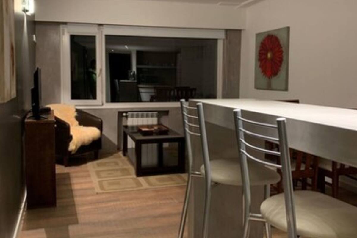 Una cocina moderna con comedor, que incluye una mesa blanca y sillas de metal, piso de madera y un ventanal grande.