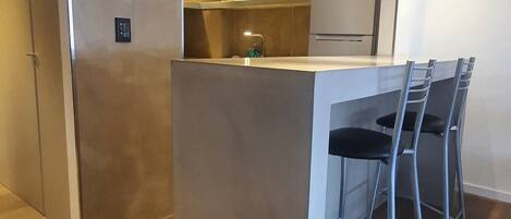 Una cocina moderna con una isla central, taburetes de bar y un refrigerador.
