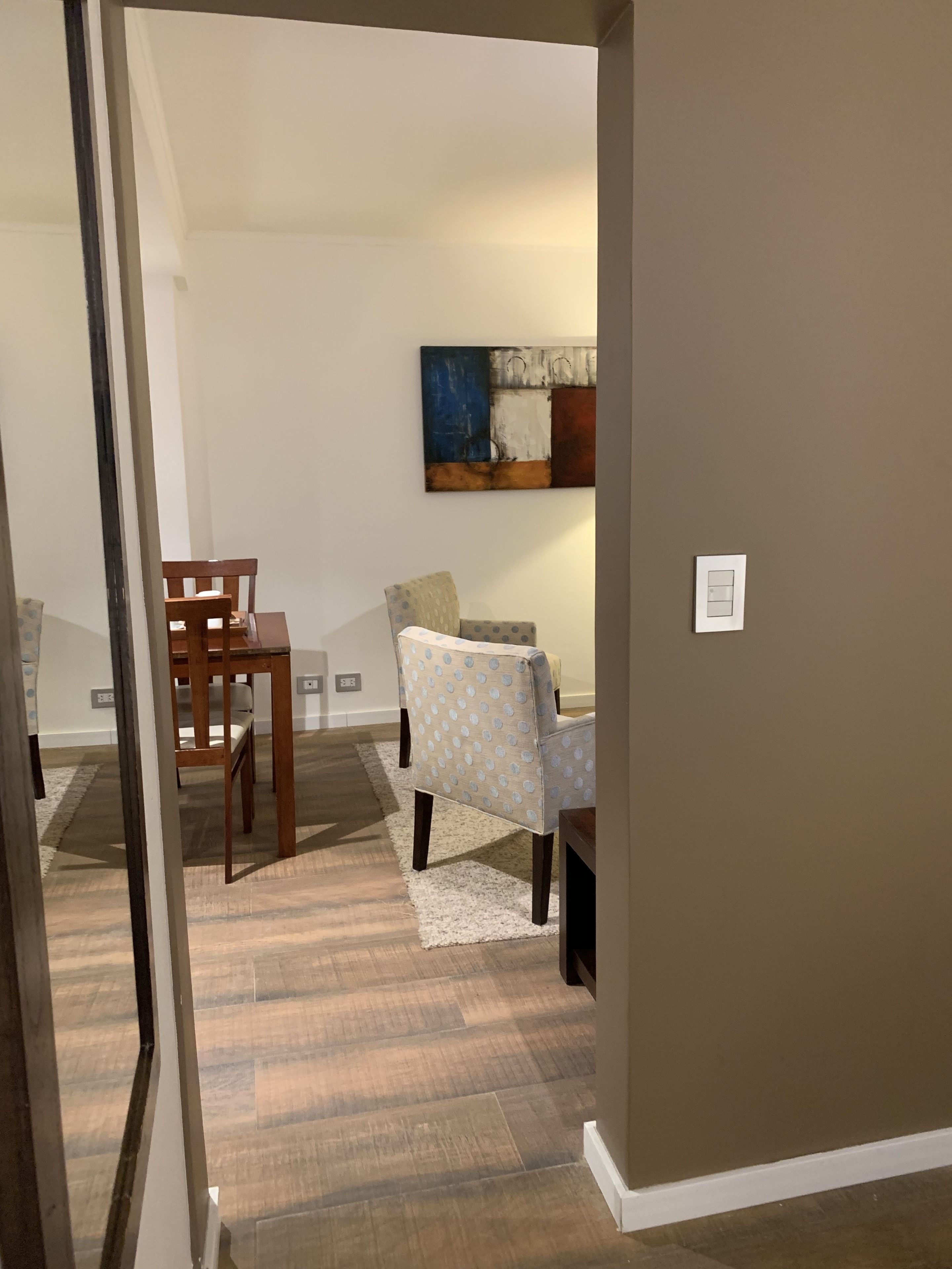 A room with a dining table, chairs, a patterned armchair, a rug, and a painting on the wall.