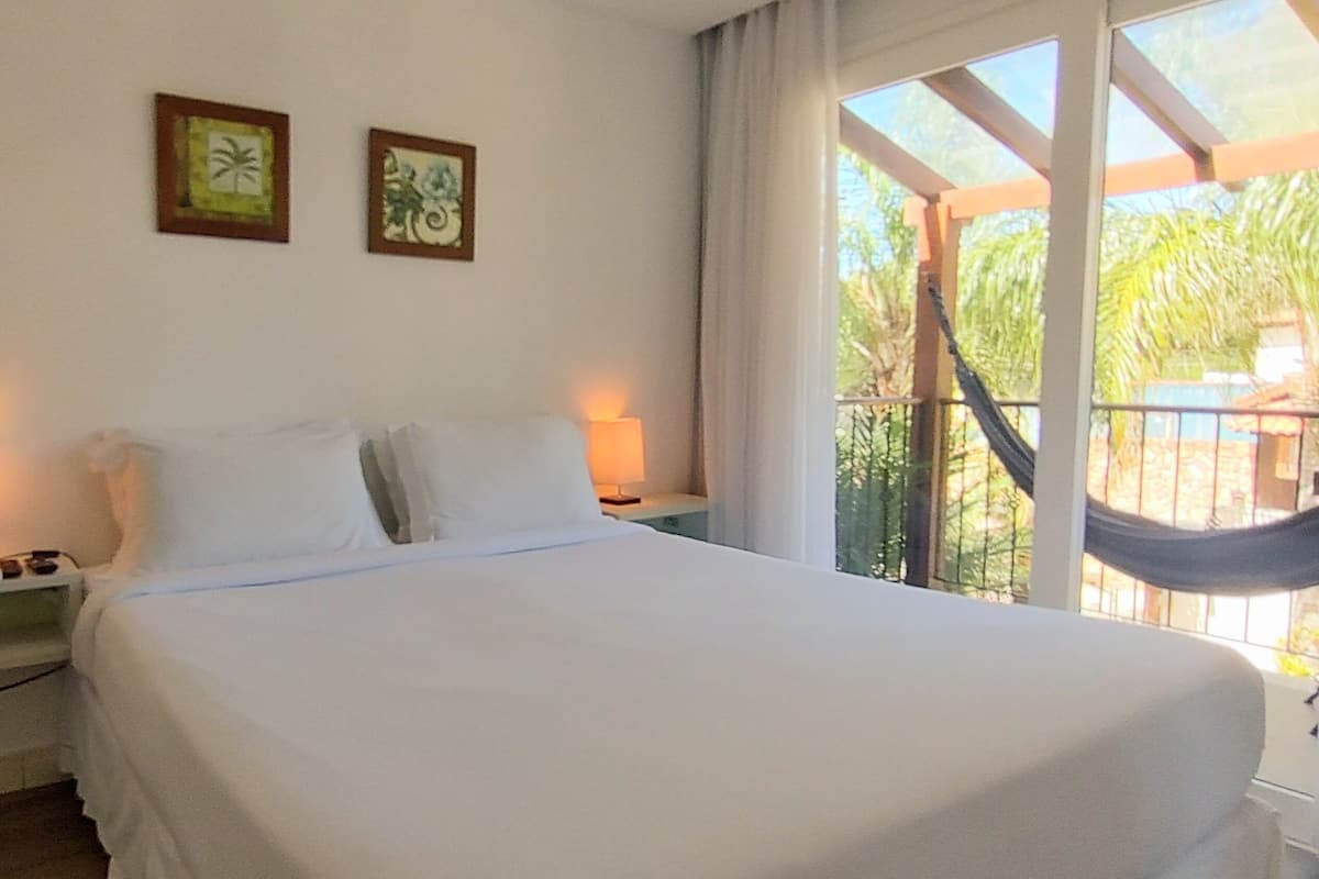 Un dormitorio con cama, dos lámparas de noche, una mesita de noche y una hamaca al lado de la ventana.
