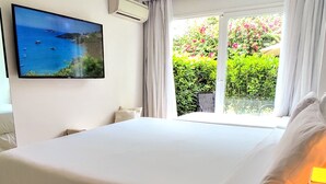 Ein Hotelzimmer mit einem großen Bett, einem an der Wand befestigten Flachbildfernseher, einem Fenster mit Vorhängen und einer Fernbedienung auf einem Nachttisch.