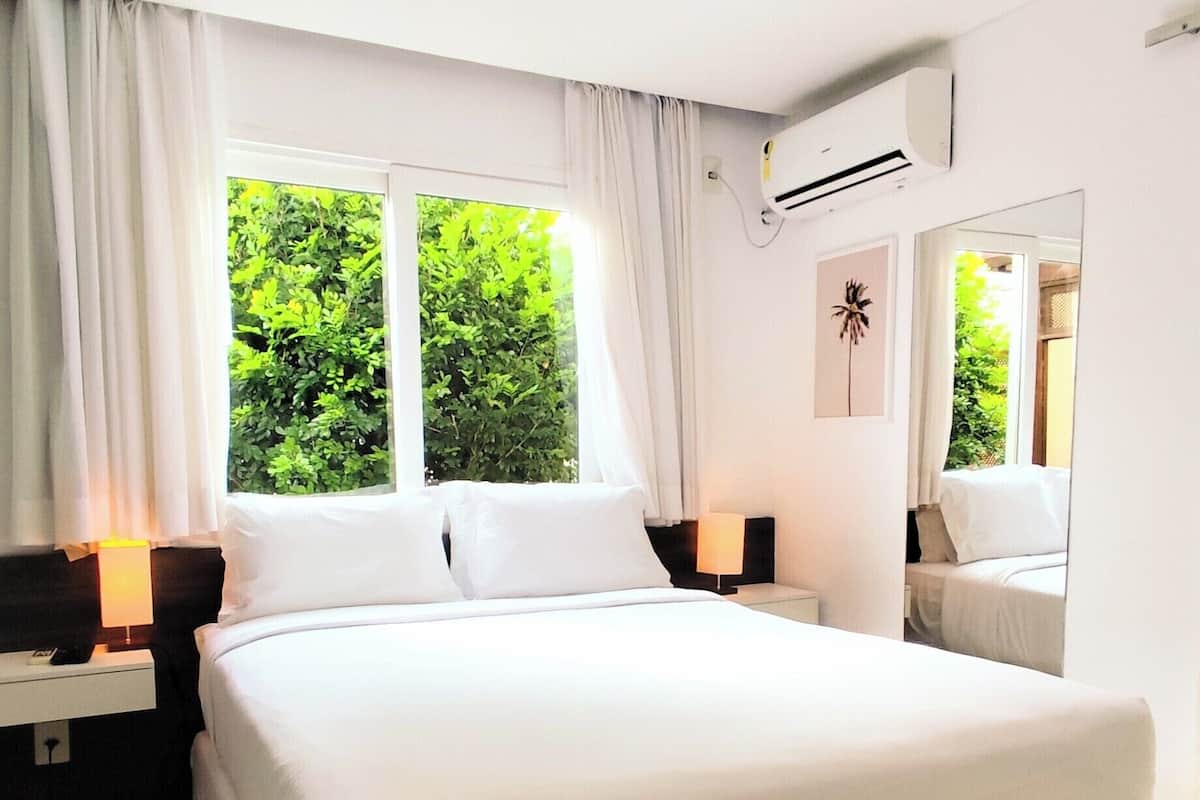 Una habitación de hotel con una cama grande, dos mesitas de noche, un ventilador de techo, una ventana con cortinas y vistas al exterior.