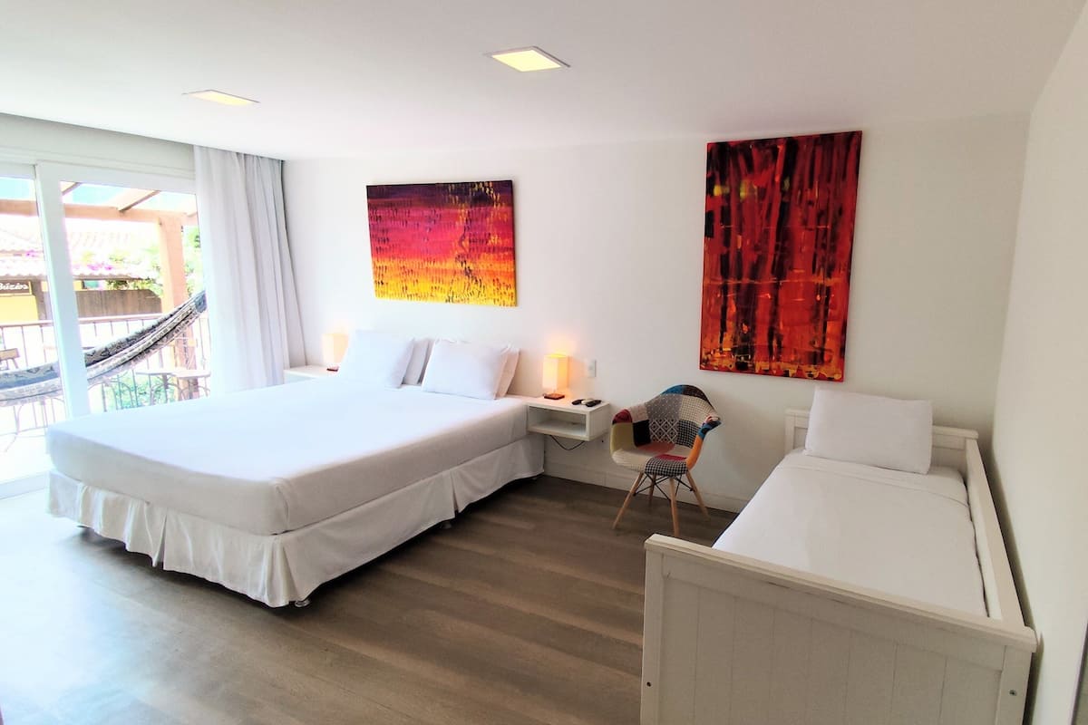 Habitación de hotel con una cama grande, una mesita de noche pequeña con una lámpara, una silla y dos cuadros abstractos en las paredes.