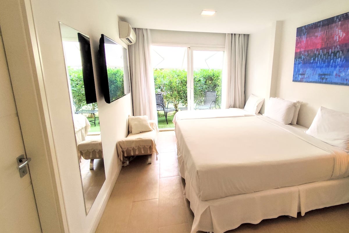 Habitación de hotel con una cama grande, un televisor montado en la pared, un cuadro y vistas al jardín a través de la ventana.