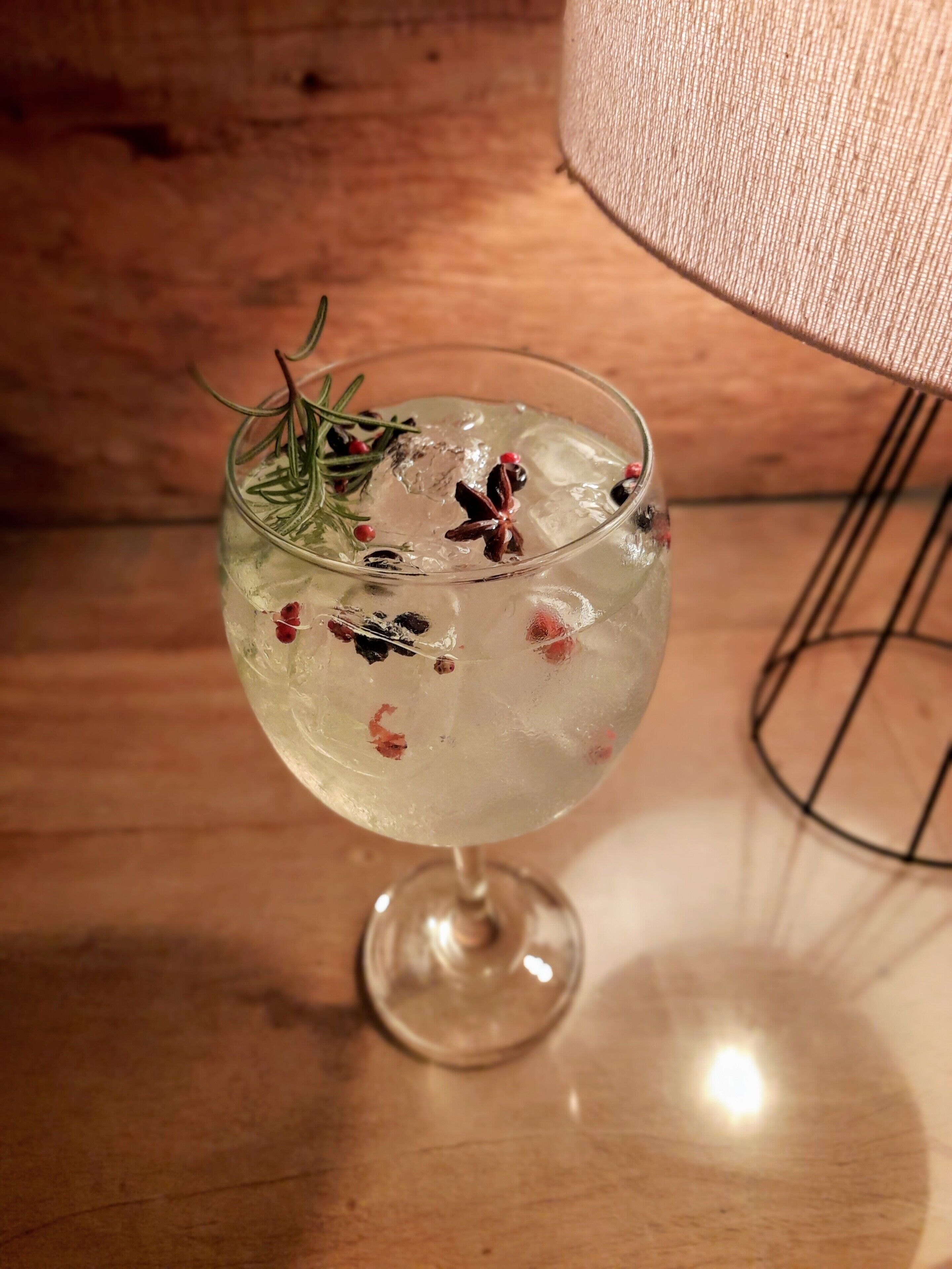 A cocktail glass with ice and garnishes on a wooden surface.