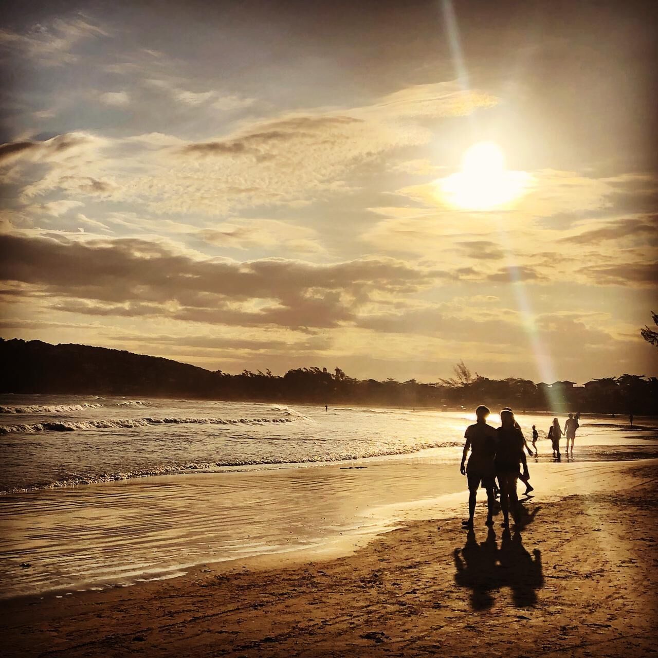 Une scène de plage où l’on voit des personnes se promener le long du rivage au coucher du soleil.