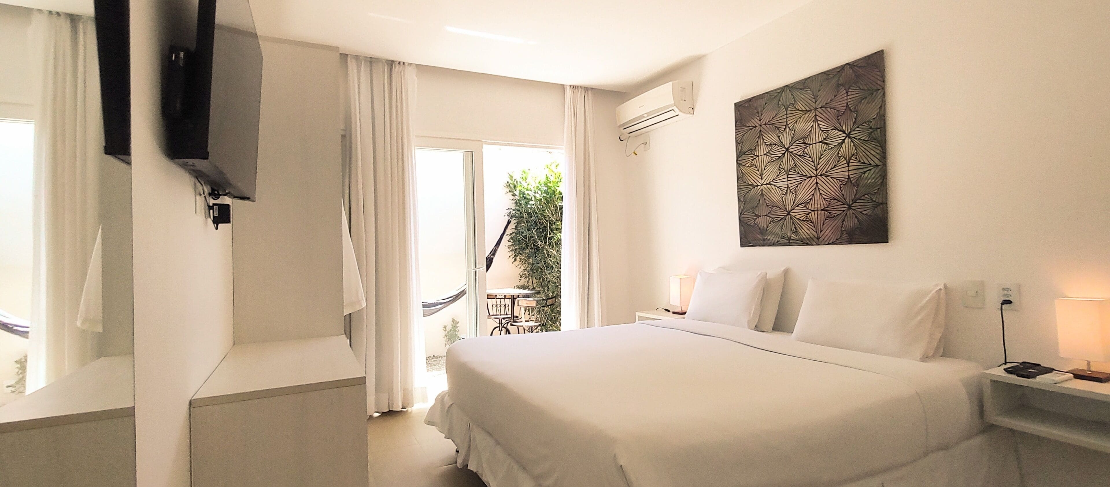 Una habitación de hotel con cama, televisión, escritorio con lámpara y ventana con cortinas.