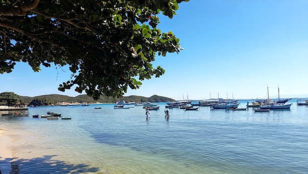 Eine Küstenansicht mit Booten, die an einem Steg festgemacht sind, klarem Wasser und einem Sandstrand.