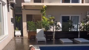 Ein Poolbereich mit einer Person, die am Pool entspannt, umgeben von Liegestühlen und Blumentöpfen.