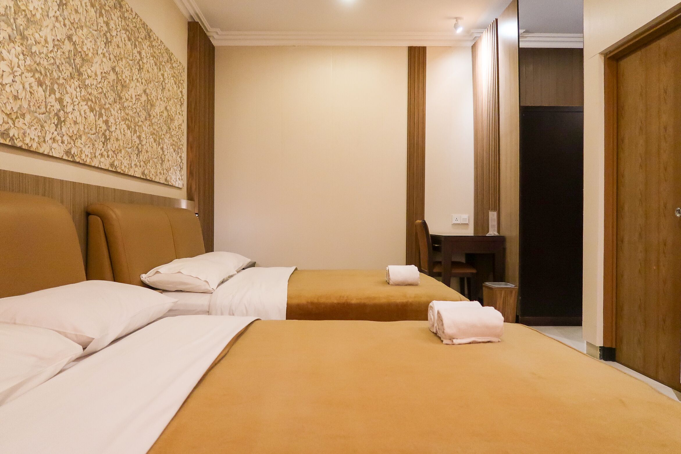 Habitació d'hotel amb dos llits, un escriptori, una cadira i una obra d'art floral gran a la paret.