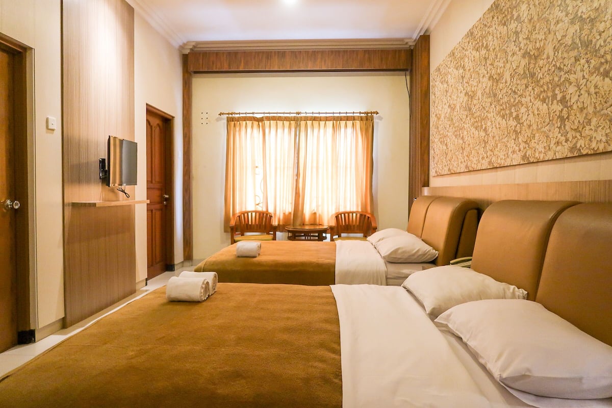 A hotel room with two beds, a television, a desk, and a window with curtains.