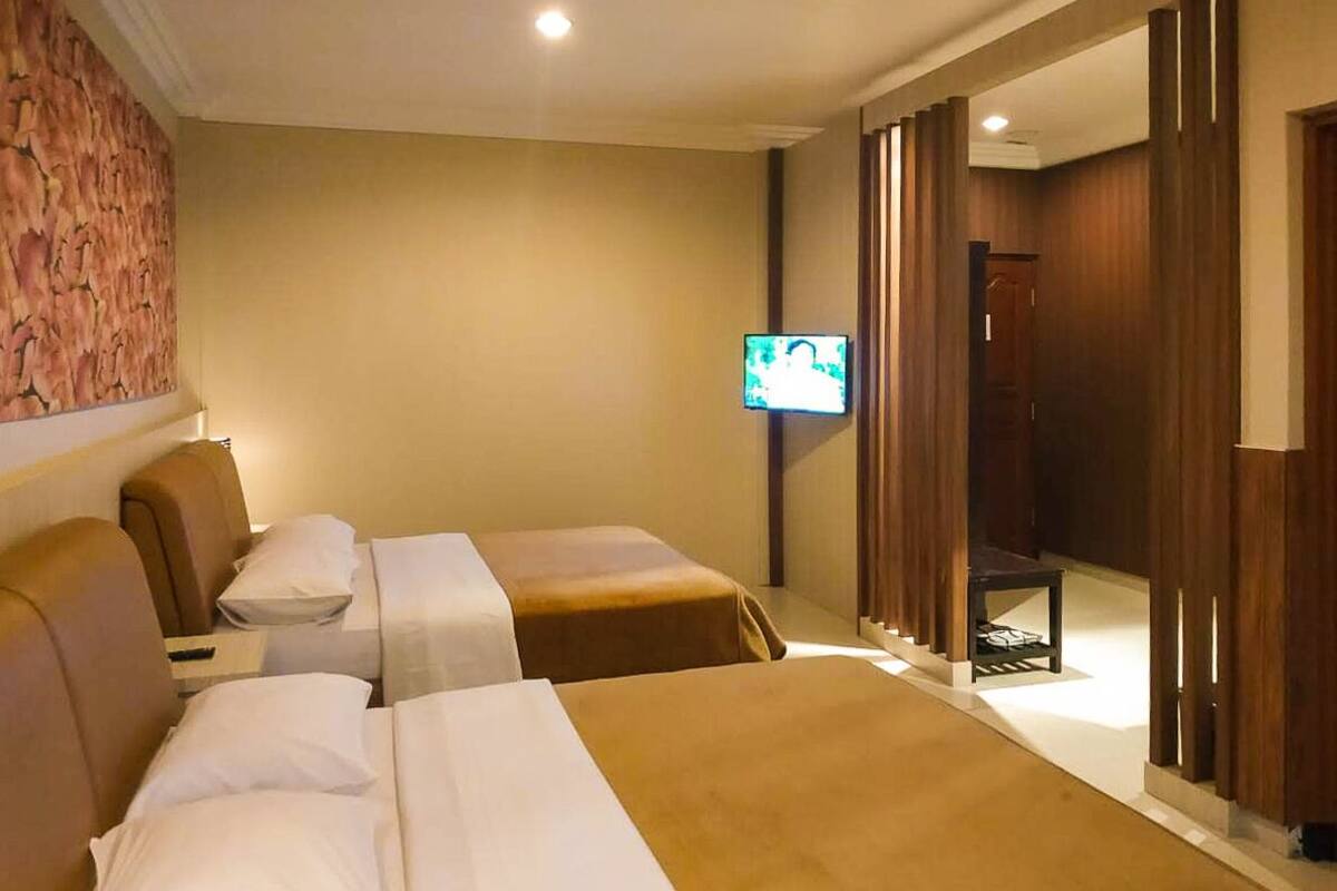 A hotel room with two beds, a television, and a wooden wardrobe.