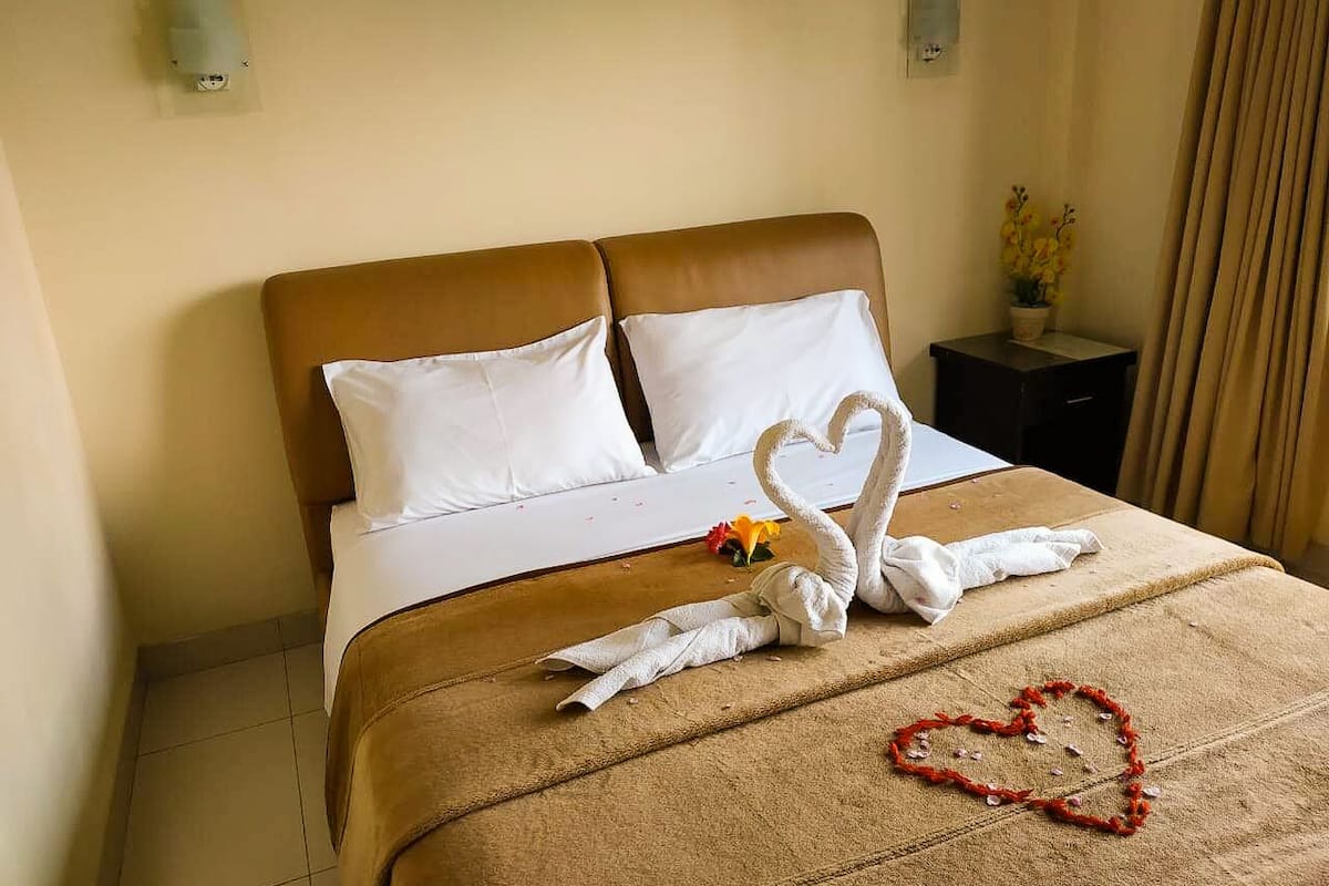 A hotel room with a neatly made bed, a heart-shaped decoration on the bed, and a swan towel art.
