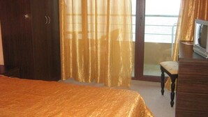A hotel room with a bed, a desk, a chair, and a view of the sea through large windows. - Hotel Blian (Ravda)