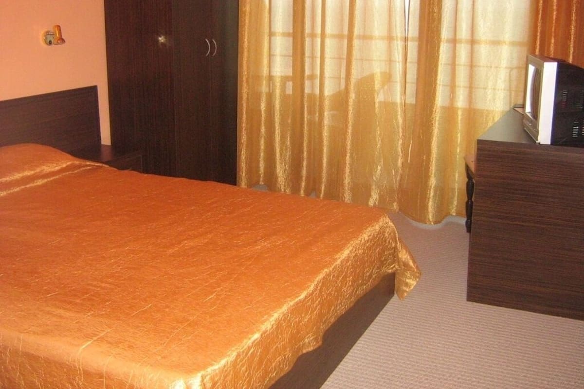 A hotel room with a bed, a wooden dresser, and a television on a stand.