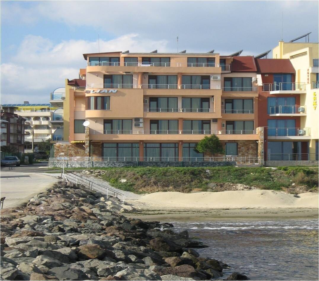 Un hotel de varios pisos con balcones, situado cerca de una costa rocosa.