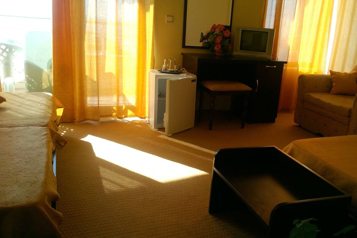 A hotel room with a bed, a desk with a computer, a chair, a sofa, and a small table.