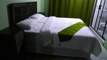 A bed with a white and green bedspread, a dark headboard, and a nightstand with a basket.