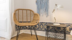A wicker chair, a table with a lamp, and a wall with blue and white tiles.